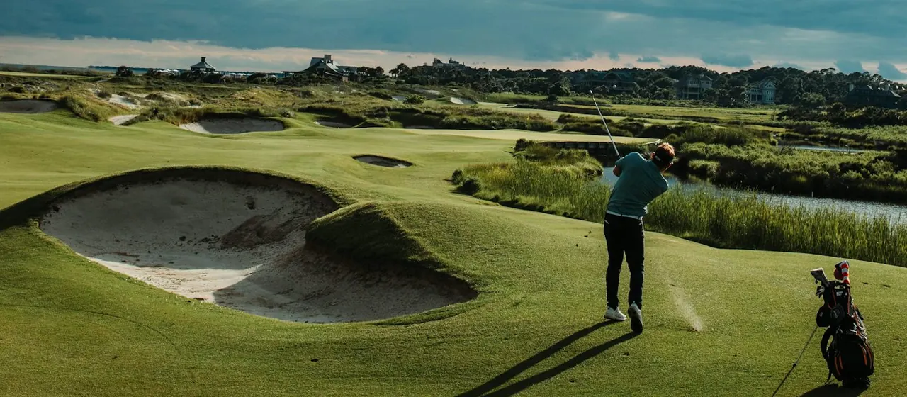 A golfer playing out of a links fairway under a dramatic sky